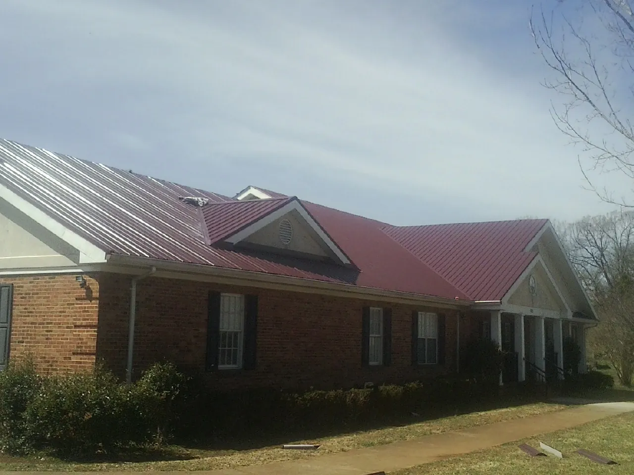Red metal roof with gabled entries on a long brick building, from a Hail Damage Roof Repair job in Scarborough