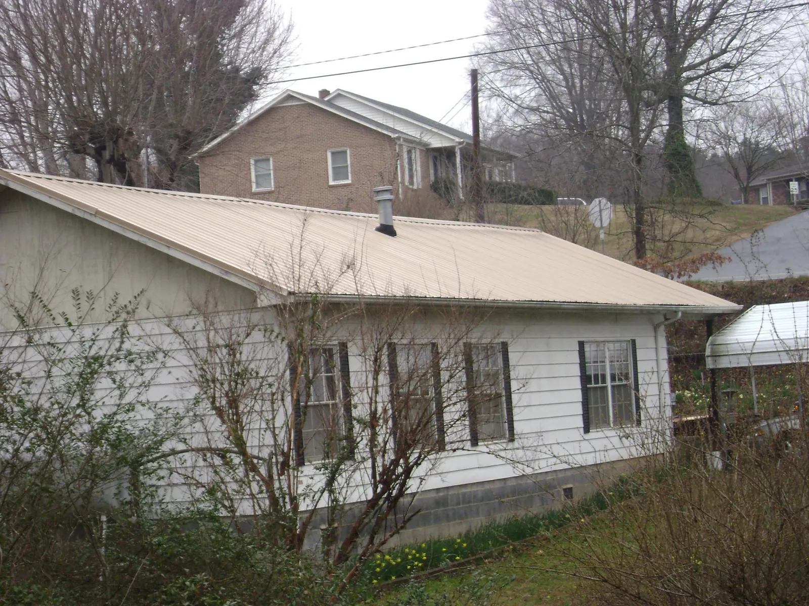 Tan metal roof on a white sided house set into a hillside — Commercial Roofing by Roofing Brothers in Scarborough